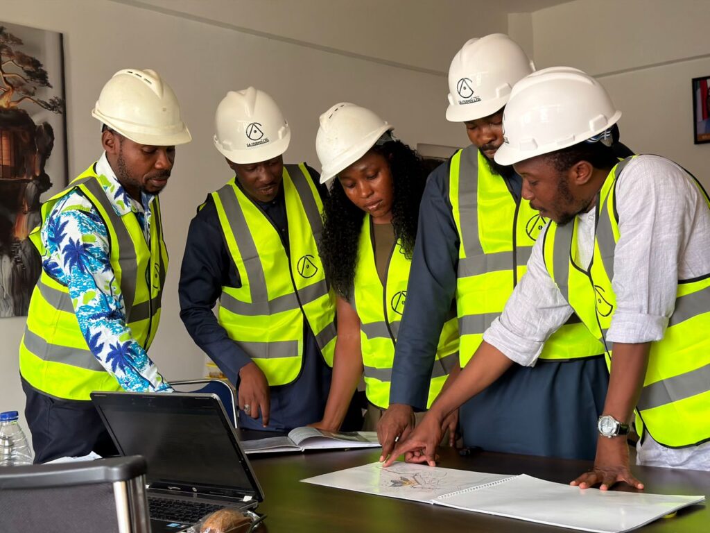 Group of engineers in safety gear reviewing blueprints indoors.